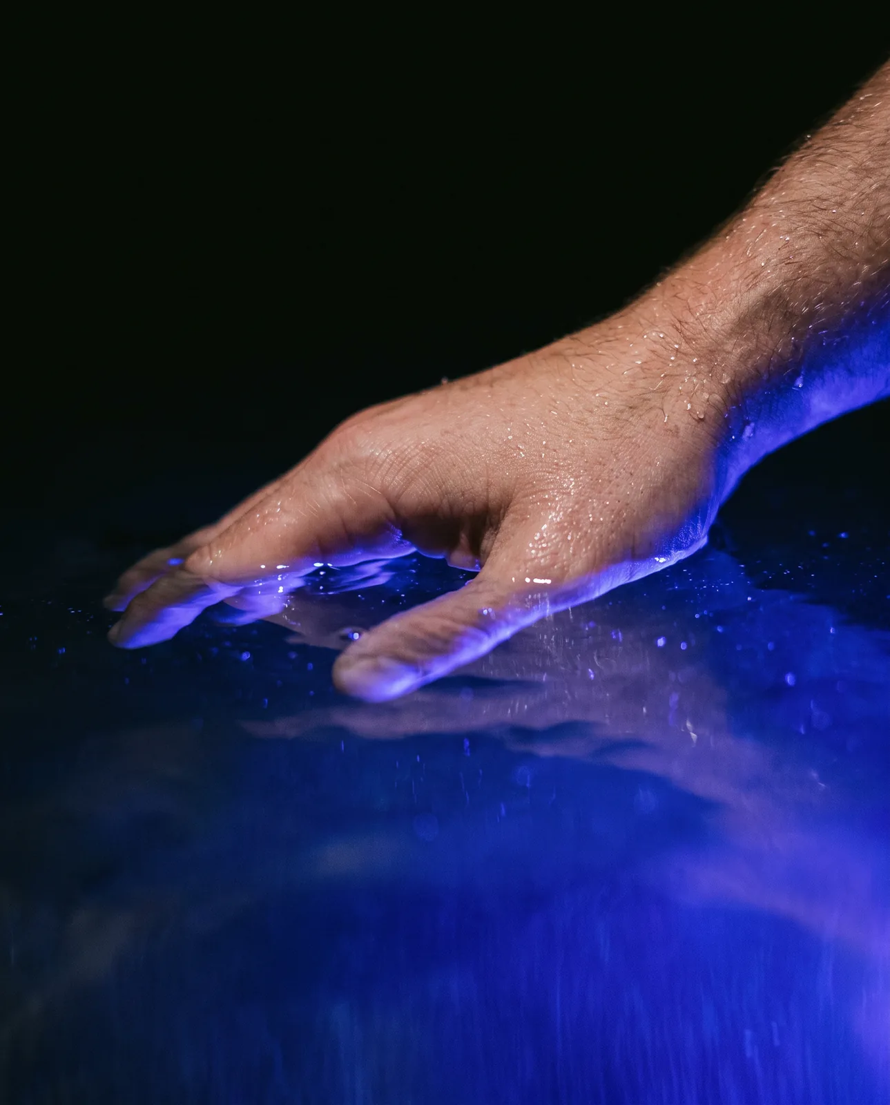 Una mano che sfiora la superficie dell'acqua illuminata di blu