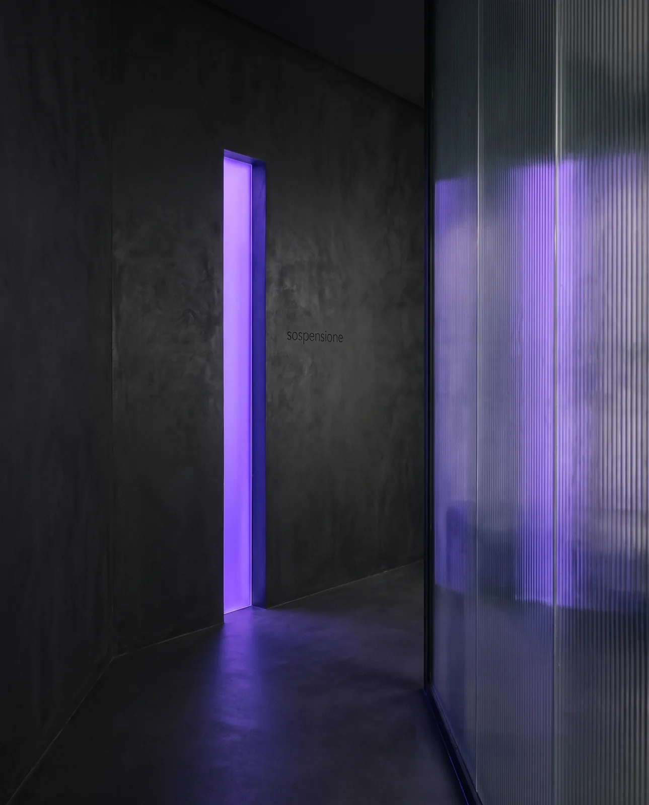 Un corridoio di cemento con una porta che è una lama di luce viola